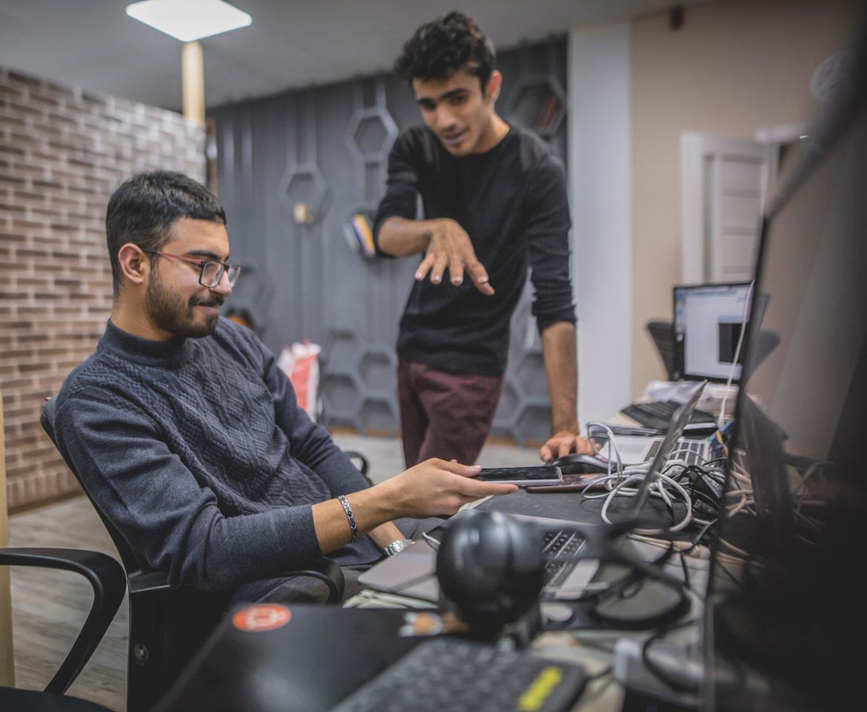2 men talking whilst looking at a laptop screen