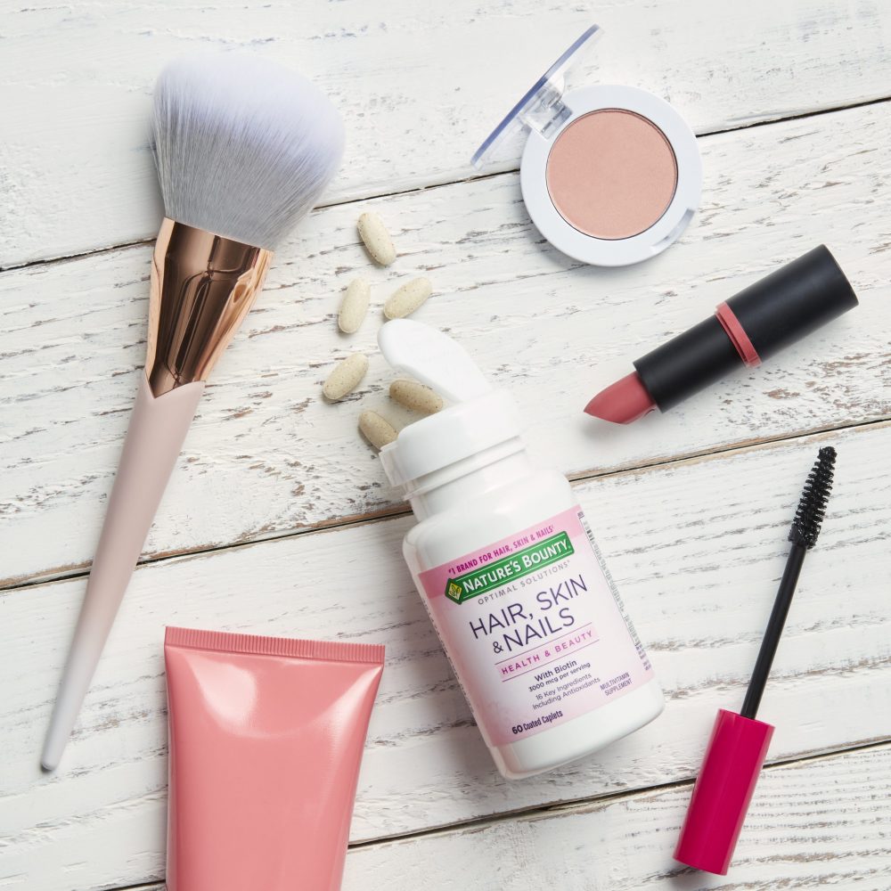 Hair skin and Nail tablets on a marble table surrounded by makeup products