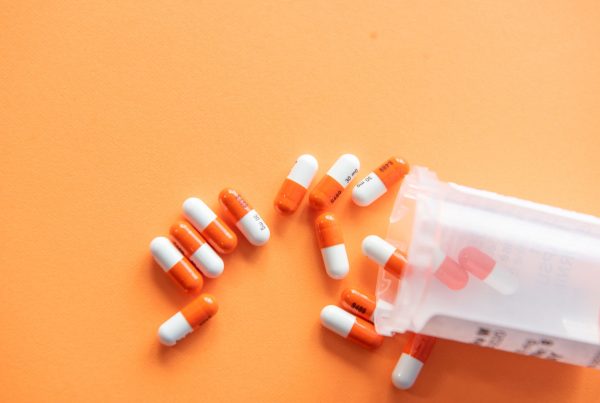 Bright orange background with some orange and white pills coming out of a medical bottle
