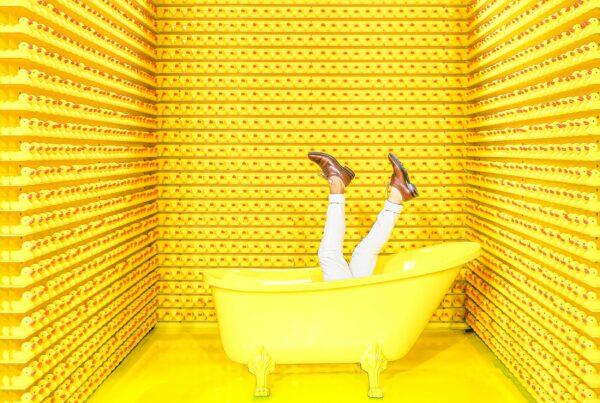 Yellow room, bathtub, legs coming out of the bath and the walls are lined with rubber ducks